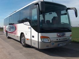 Weiß-roter Reisebus auf einer Landstraße vor grünem Feld und blauem Himmel.