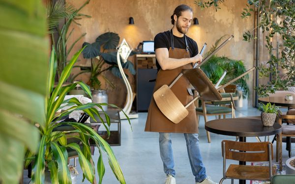 Ein Servicemitarbeiter in der Gastronomie bestuhlt die Tische in einem Restaurant.