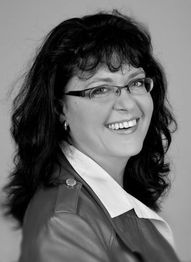 Eine lächelnde Frau mit Brille und Lederjacke, in Schwarzweiß fotografiert.