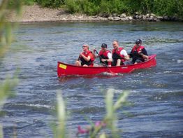 Vier Personen paddeln in einem roten Kanu auf einem Fluss.