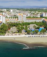 Vista aérea de un resort frente a una playa, rodeado de vegetación y edificios altos al fondo.