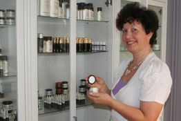 Eine Frau steht vor einem Regal mit Kosmetikprodukten und hält eine Cremedose in der Hand.