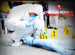 Investigador en traje forense examina un cuerpo rodeado de marcadores de evidencia numerados.