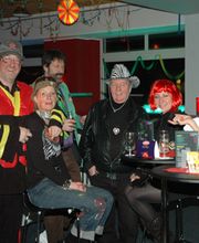 Gruppe von Leuten in Kostümen bei einer Feier, stehen um einen Tisch mit Getränken.