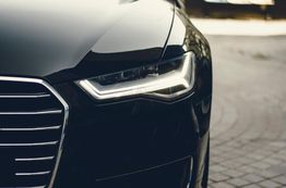Close-up of a sleek black car's front grille and headlight, parked on cobblestone pavement.