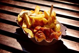 Currywurst und Pommes mit Mayo in einer Schale auf Holztisch bei Sonnenlicht.