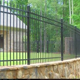 Black iron fence with stone base, enclosing a green lawn near a house and tall trees.
