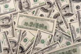 A scattered pile of US one hundred dollar bills featuring Benjamin Franklin's portrait.