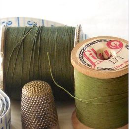 Spools of green thread, a thimble, and tape measure on a sewing table.