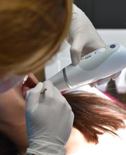 Zahnarzt untersucht mit modernem Gerät den Mund einer Patientin.