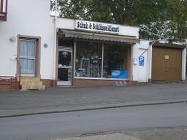Schuh- und Schlüsseldienst an einer Straße mit angrenzendem Parkplatz auf der rechten Seite.