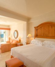 Habitación de hotel luminosa con vista al mar, cama grande y sala de estar con terraza.