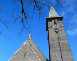 Kerk met hoge toren tegen een blauwe lucht, takken op de voorgrond.