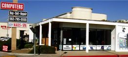 Computer store with signage on a sunny day, offering buy, sell, and repair services.