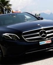 Schwarzes Mercedes-Taxi vor einer Bergkulisse mit Palmen im Hintergrund.