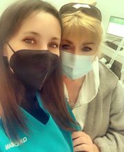 Dos personas con mascarillas en entorno clínico se toman una selfie.