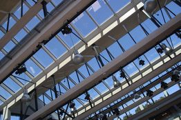 Glazen dak met metalen balken en spots, zicht op blauwe hemel.