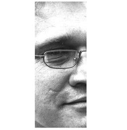 Schwarz-weiß-Nahaufnahme eines Mannes mit Brille, zeigt die rechte Gesichtshälfte und ein Lächeln.