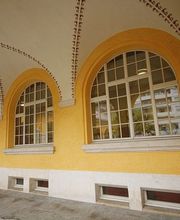 Gelber Gebäudebogen mit großen Fenstern, weißer Simse und Verzierungen an der Decke.