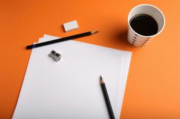 Papier, Stifte, Radiergummi, Spitzer und Kaffee auf orangefarbenem Hintergrund.