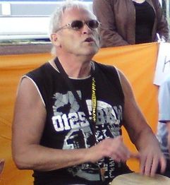 Ein Mann mit Sonnenbrille spielt Trommel, vor orangefarbenem Hintergrund.