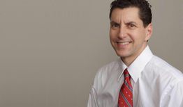 Smiling man in a white shirt and red tie against a gray background.