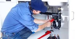 Persona reparando tuberías debajo de un fregadero con herramientas de fontanería.