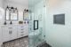 Modern bathroom with glass shower, white cabinets, dual mirrors, and patterned floor tiles.