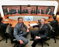 Reunião por videoconferência com cinco pessoas na tela e cinco em volta de uma mesa.