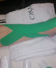 Pierna con cinta kinesiotape verde sobre una camilla blanca.