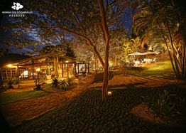 Pousada à noite, iluminação quente entre árvores e jardins bem cuidados.