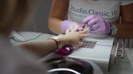 Person mit rosa Handschuhen lackiert Fingernägel einer anderen Person in einem Nagelstudio.