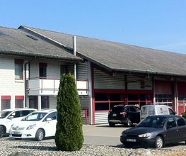 Gewerbegebäude mit mehreren Autos im Parkbereich, blauer Himmel im Hintergrund.