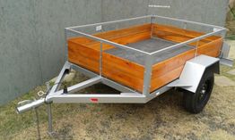 Reboque metálico com laterais de madeira, estacionado em uma superfície gramada.