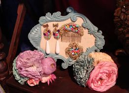 Accesorios coloridos en marco decorativo azul, rodeados de flores de tela en tonos pastel.