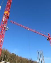 Zwei rote Baukräne heben Baumaterial in den blauen Himmel über einer Baustelle.