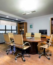 Sala de reuniões elegante com mesa oval, cadeiras estofadas e estante ao fundo.