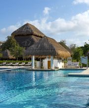 Piscina amplia con tumbonas y edificios de techo de paja rodeados de vegetación.