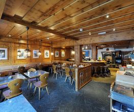 Gemütliches Restaurant mit Holzwänden, Tischen und Stühlen. Bilder an den Wänden.