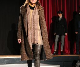 Frau trägt Winterkleidung auf dem Laufsteg: Mantel, Mütze, Schal und Stiefel.