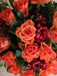 Ein Strauß mit orangefarbenen Rosen und roten Beeren, umgeben von grünen Blättern.