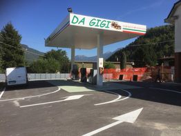 Stazione di servizio "Da Gigi" in montagna, con un furgone e segnaletica stradale bianca.