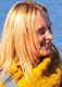 Blonde Frau mit gelbem Schal lächelt im Profil vor einem blauen Hintergrund.