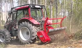 Red tractor with mulcher clearing land in a forested area.