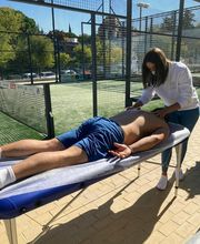 Persona recibiendo masaje al aire libre en una camilla, cerca de una pista de pádel.