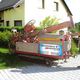 Mann bedient Bohrmaschine im Garten vor gelbem Haus. Schild: "Brunnenbau & Bohrservice".