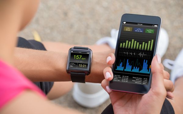 Frau schaut auf Smartwatch und Smartphone, um Gesundheitsdaten zu erhalten