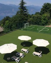 Liegestühle und Sonnenschirme auf einem Platz mit Kunstrasen, dahinter ein kleiner Fußballplatz.