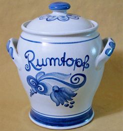 Keramiktopf mit blauer Dekoration und Aufschrift "Rumtopf" auf beigefarbenem Hintergrund.
