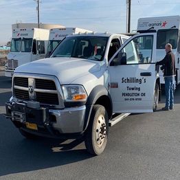 Tow truck with "Schilling's Towing" on the side, parked near Aramark trucks, man beside it.